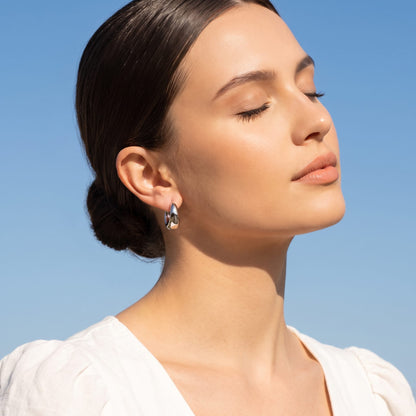 Woman wearing the Nina dome huggie silver earrings on the ear facing up