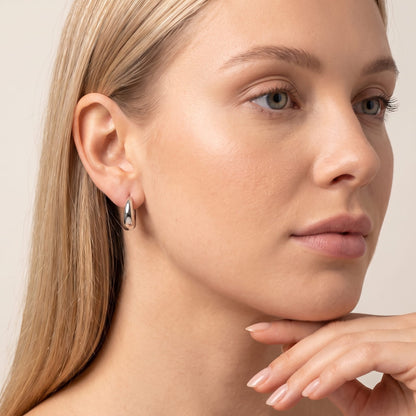 Woman wearing the Nina dome huggie silver earrings on the ear resting chin