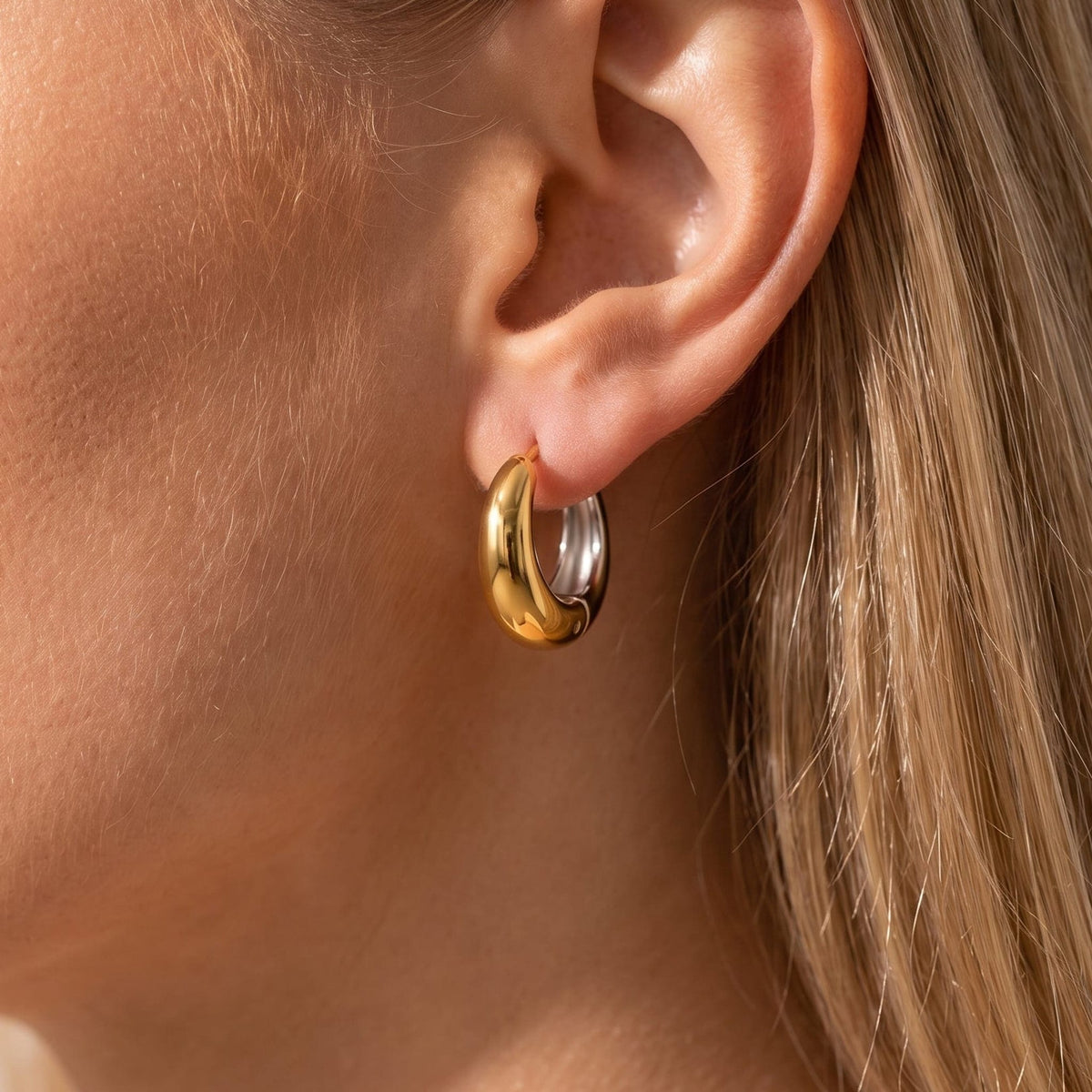 Woman wearing the Nina dome huggie two-tone earrings on the ear