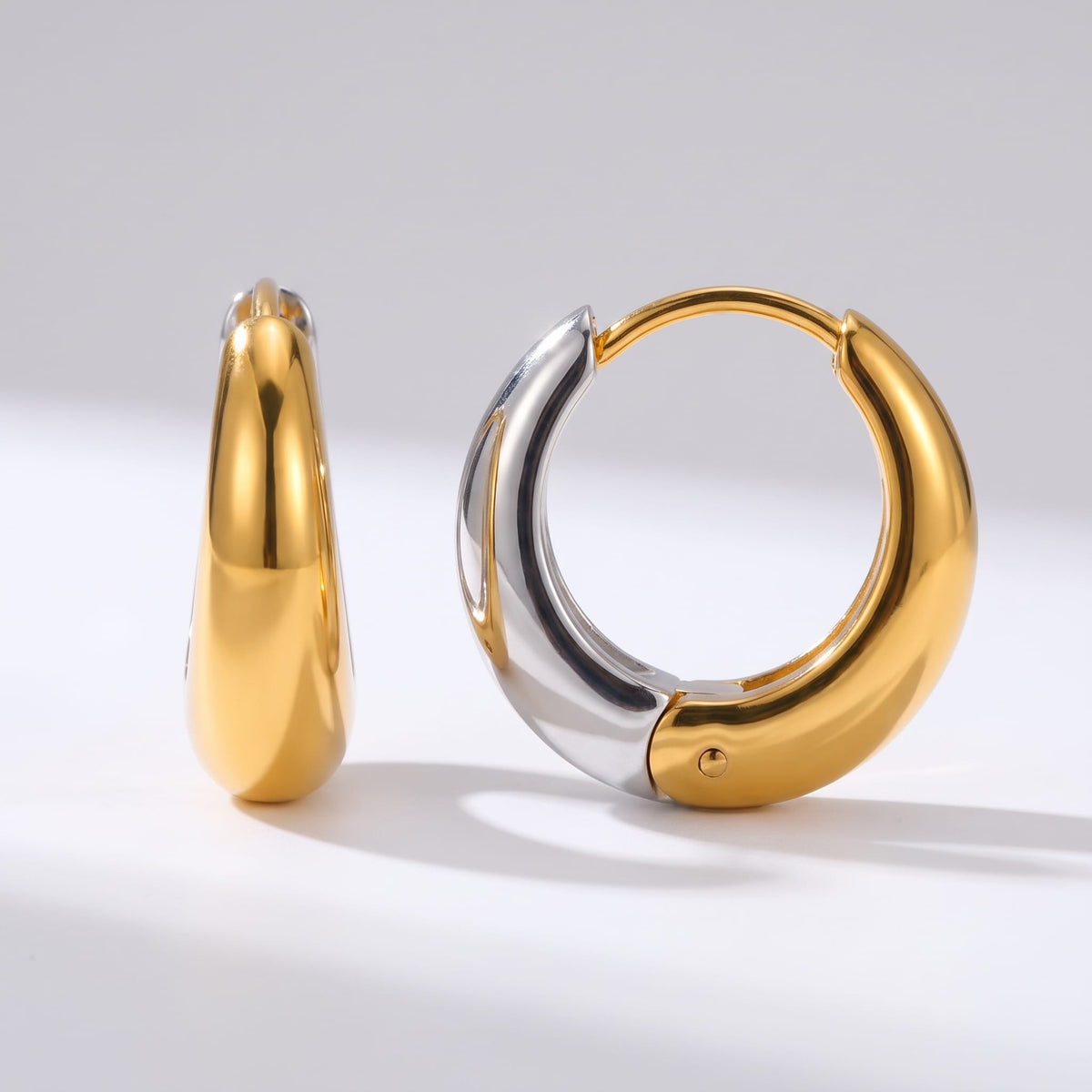 Nina dome huggie two-tone earrings on a white surface in bright studio lighting
