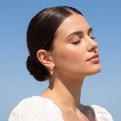 Woman wearing the Nina dome huggie two-tone earrings on the ear against a blue sky