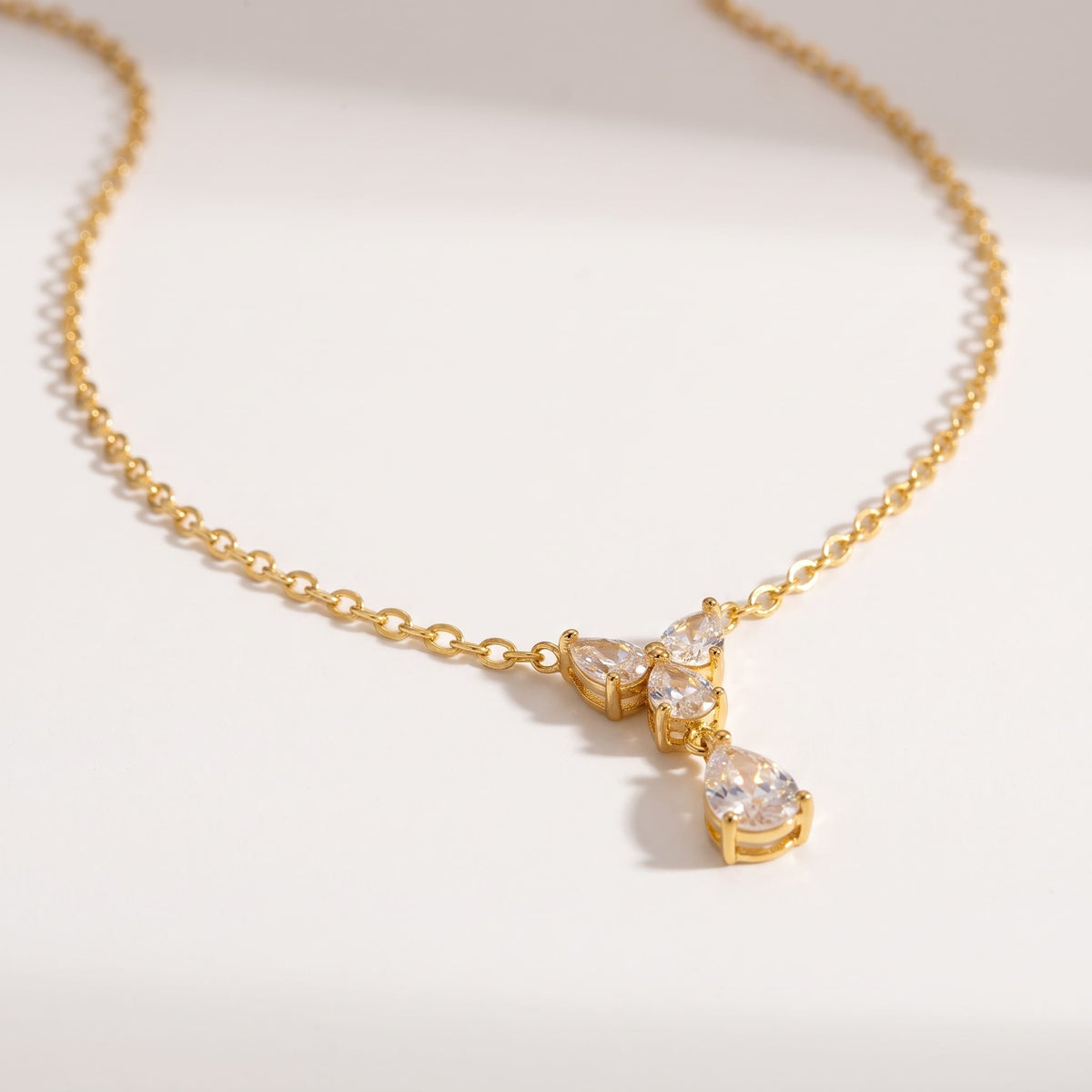 Noémie crystal teardrop gold necklace on a white surface with soft light and delicate shadows