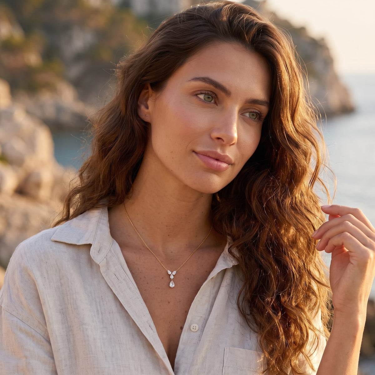 Woman wearing the Noémie crystal teardrop gold necklace at the collarbone in an unbuttoned shirt outdoors