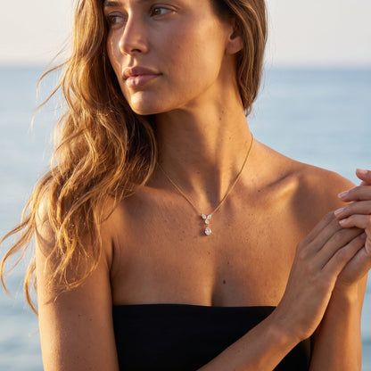 Woman wearing the Noémie crystal teardrop gold necklace at the collarbone posing near the ocean water