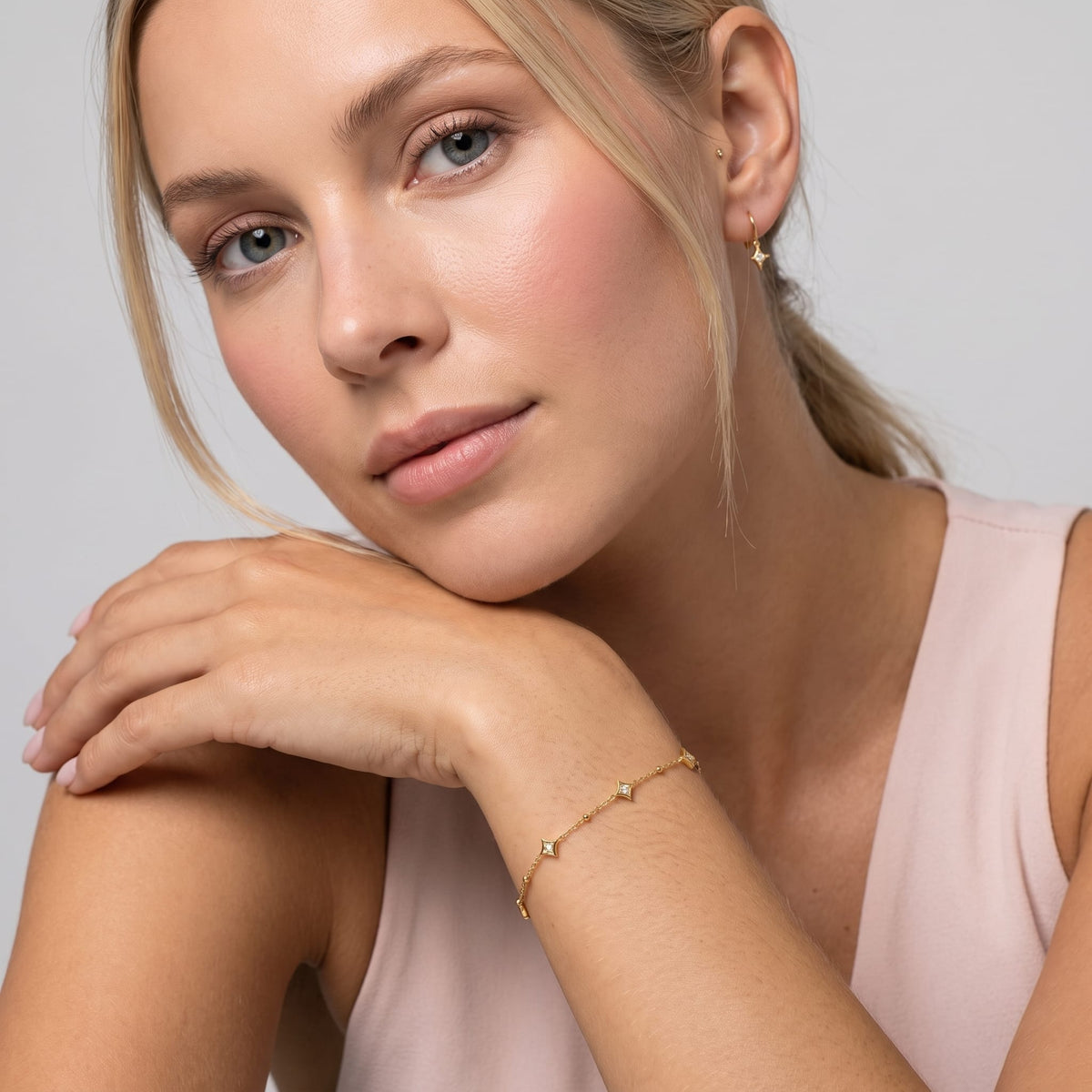 Woman wearing the Océane star station gold bracelet on the wrist resting her chin on her hand
