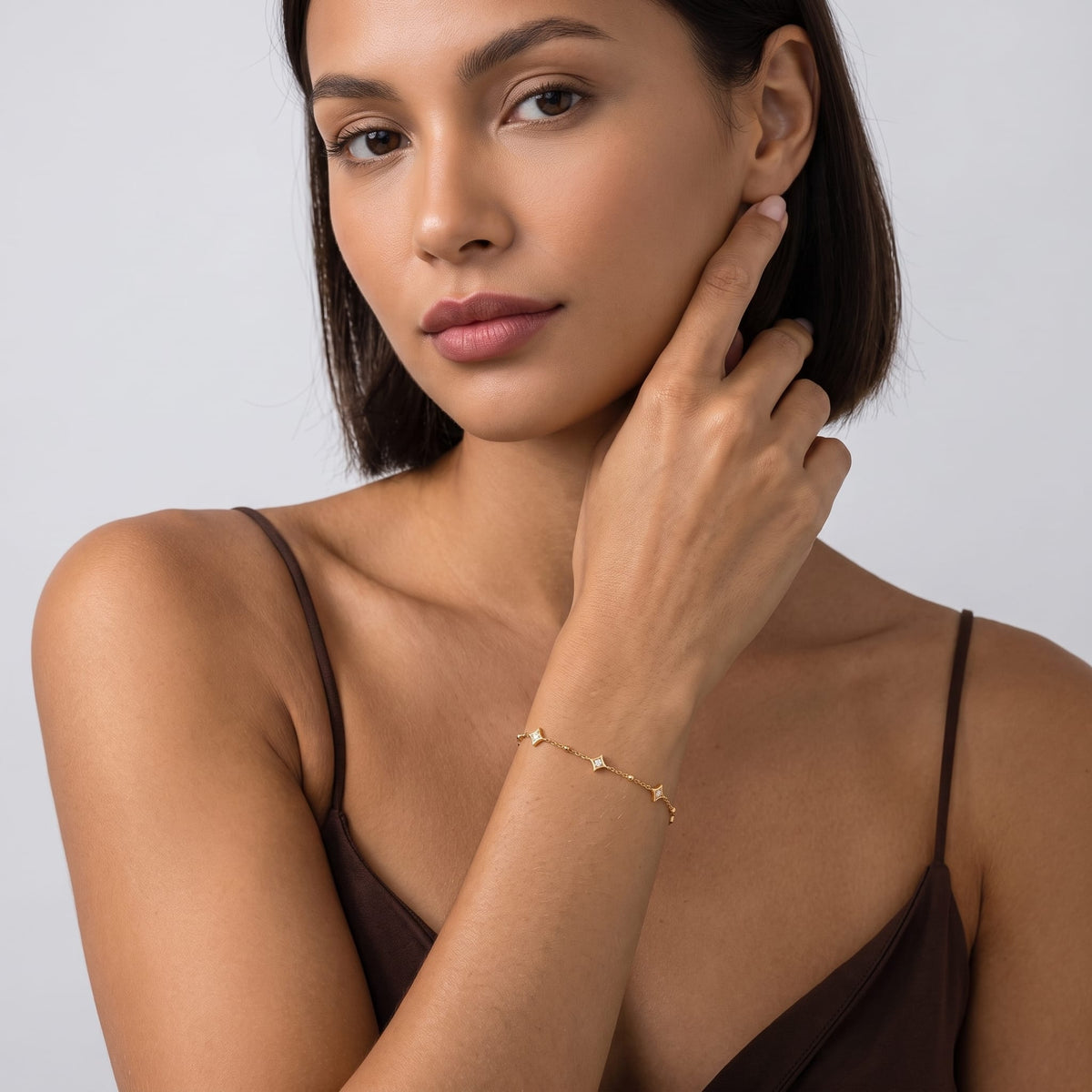 Woman wearing the Océane star station gold bracelet on the wrist touching her jawline in dark clothing