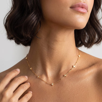 Woman wearing the Océane star station gold necklace at the collarbone with her hand raised