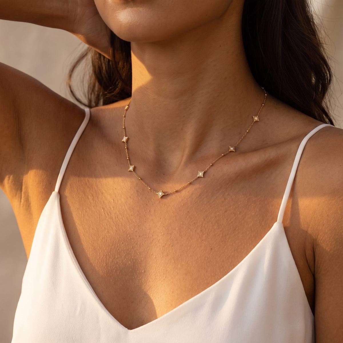 Woman wearing the Océane star station gold necklace at the collarbone in a white camisole