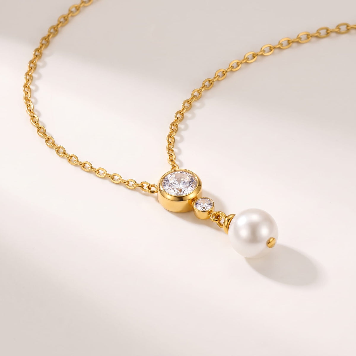 Odette crystal pearl gold necklace on a white surface displaying the faux pearl drop pendant
