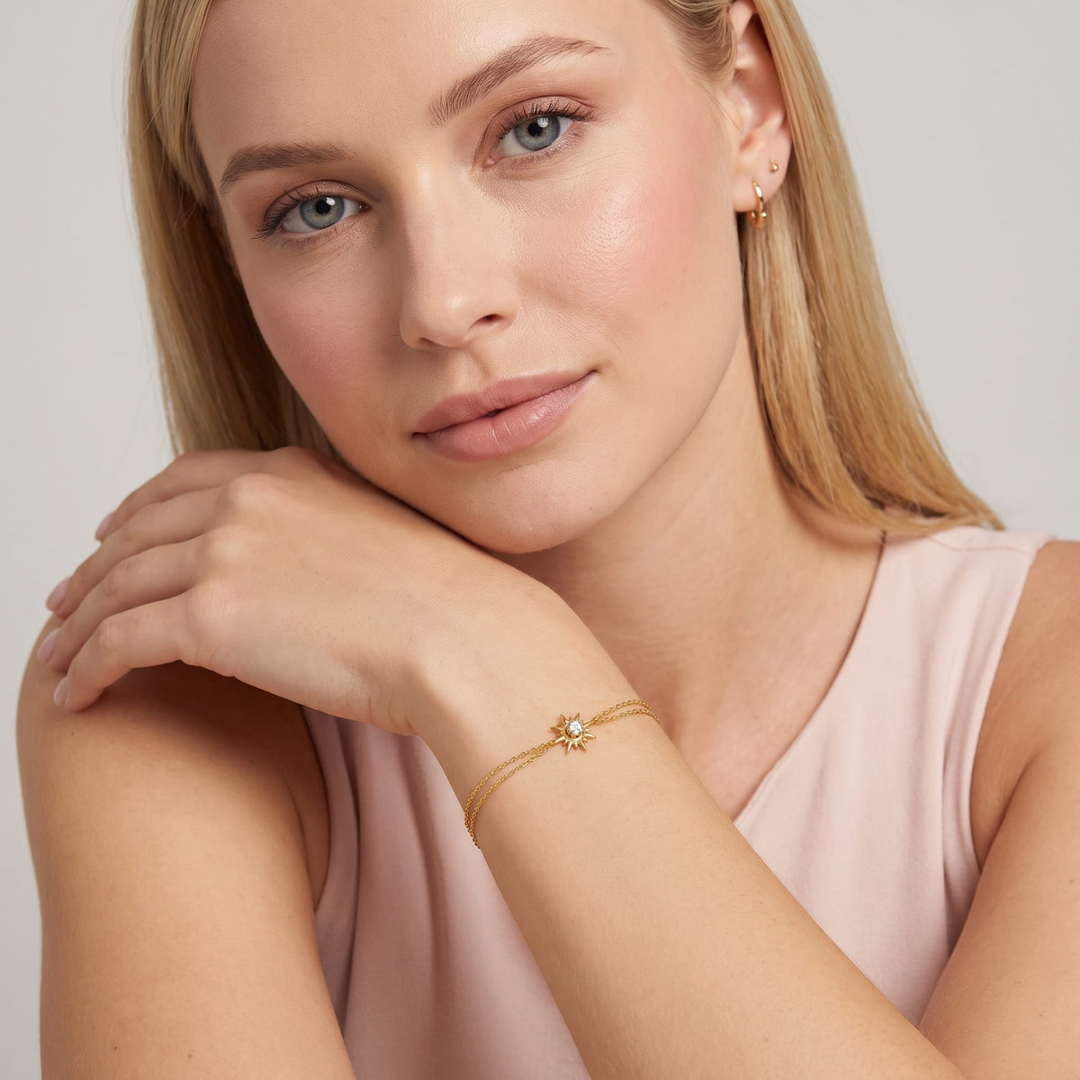 Woman wearing the Olivia crystal sun gold bracelet on the wrist resting her head on her hand