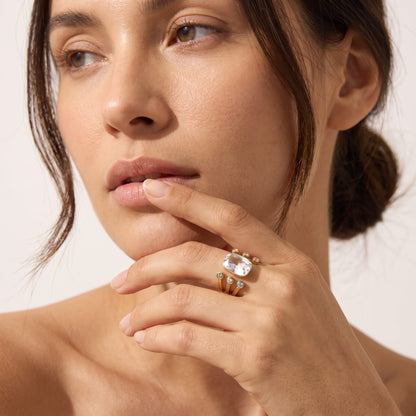 Close-up of a woman's face and hand wearing the Olivia cushion crystal gold ring