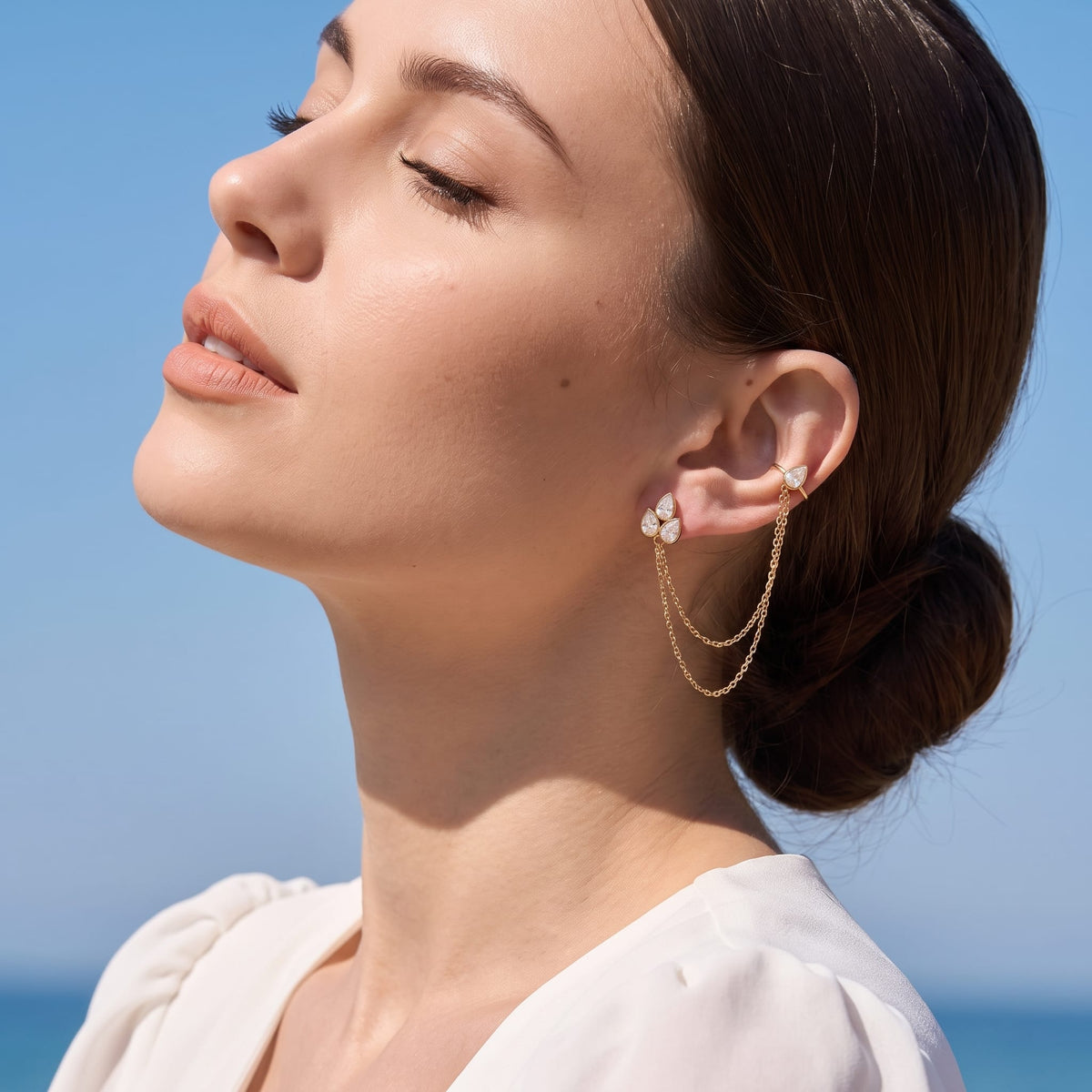 Woman wearing the Ophélie cuff chain gold earrings on her ear with eyes closed in sunlight
