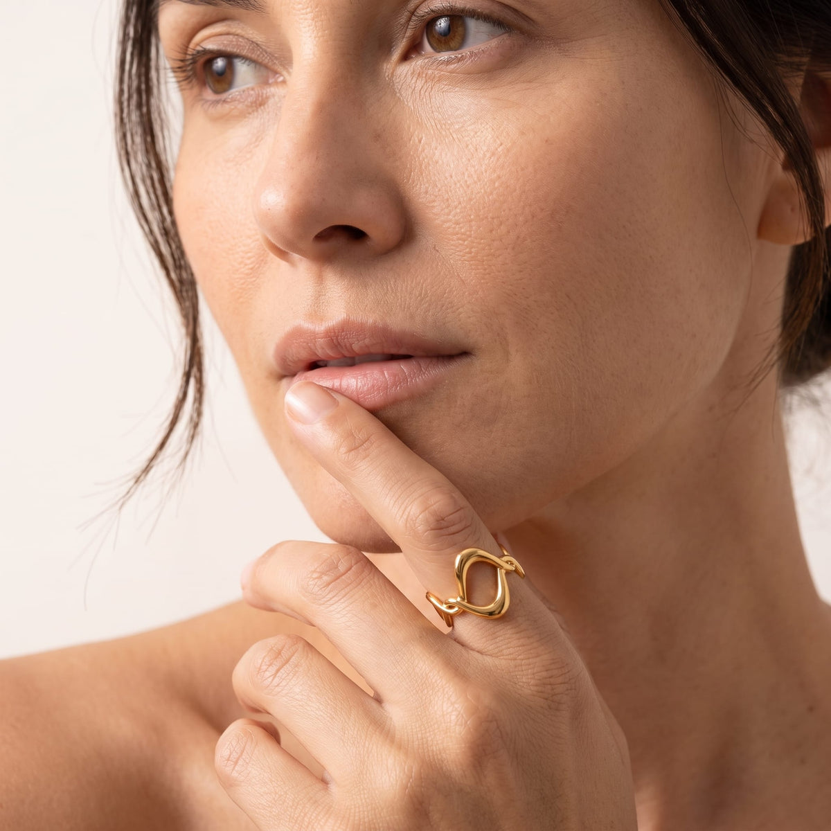 Woman wearing the Ophélie twisted wave gold ring on the hand posing near her chin