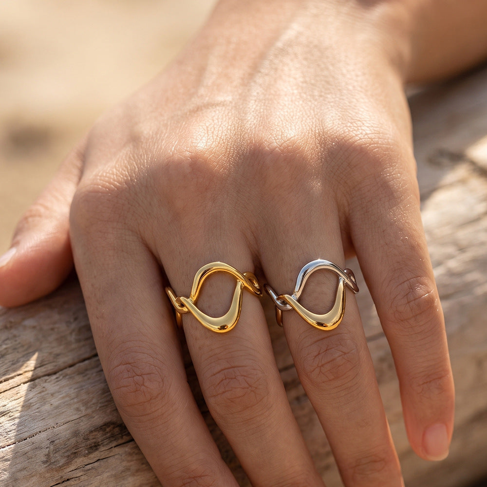 Ophélie two-tone ring worn on the ring finger beside the gold version, hand resting on driftwood