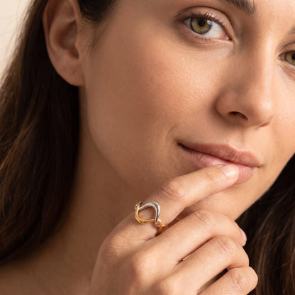 Woman wearing the Ophélie twisted wave two-tone ring on the hand touching her lip in a close-up shot