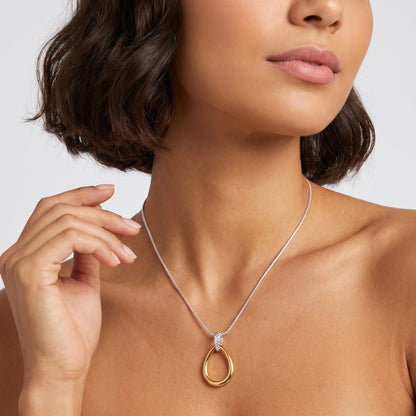 Woman wearing the Oriane open teardrop two-tone necklace at the throat lifting one hand to her hair