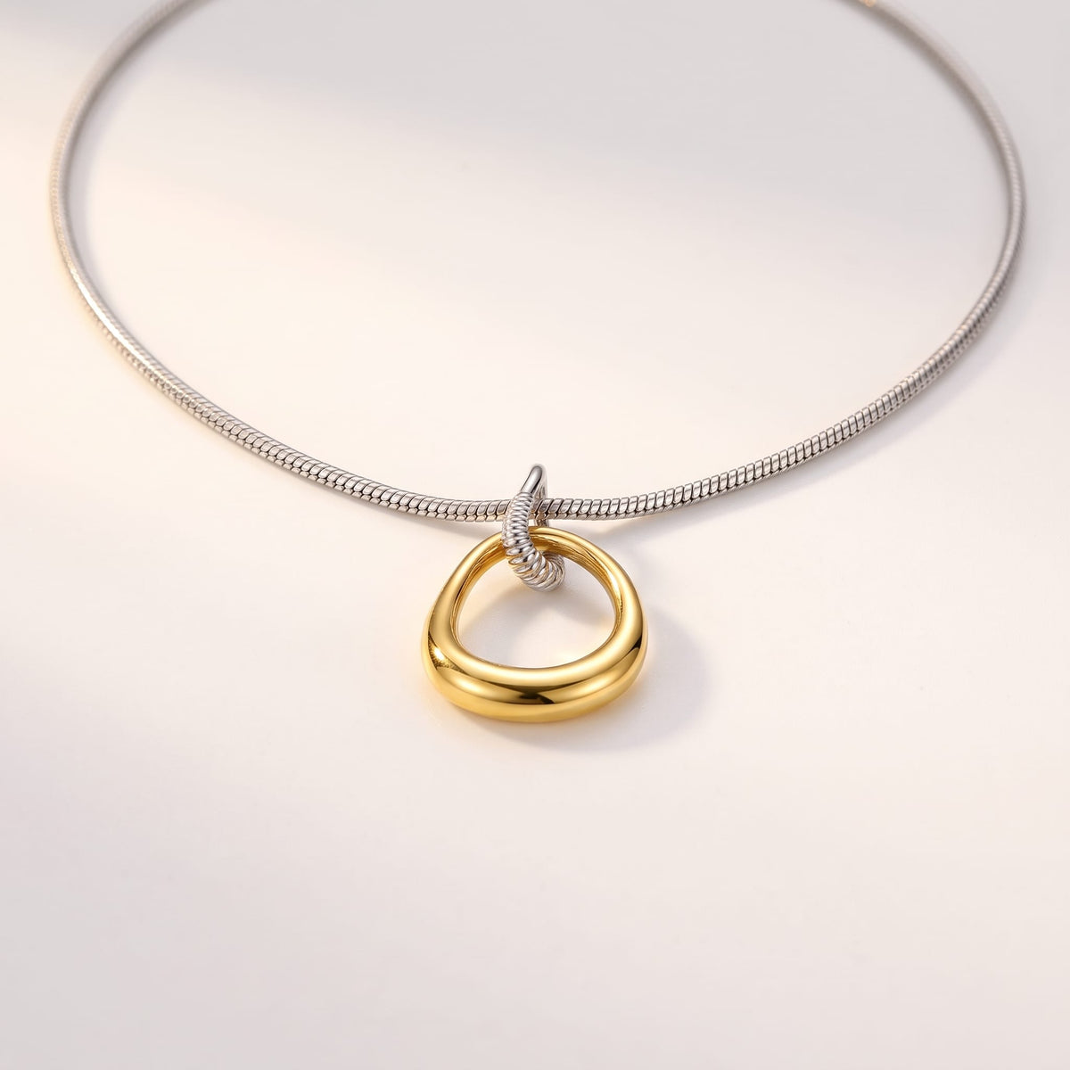 Oriane open teardrop two-tone necklace on a light background illuminated by soft sunlight