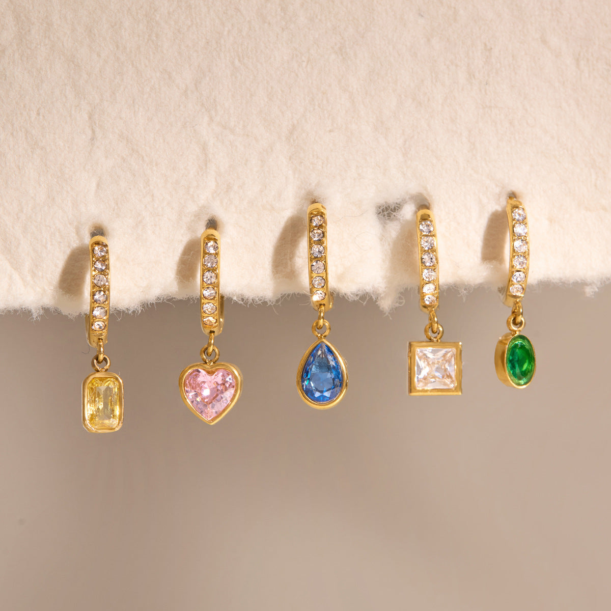 Paola blue teardrop earring in the middle of a row of five colored crystal huggies hung from soft paper