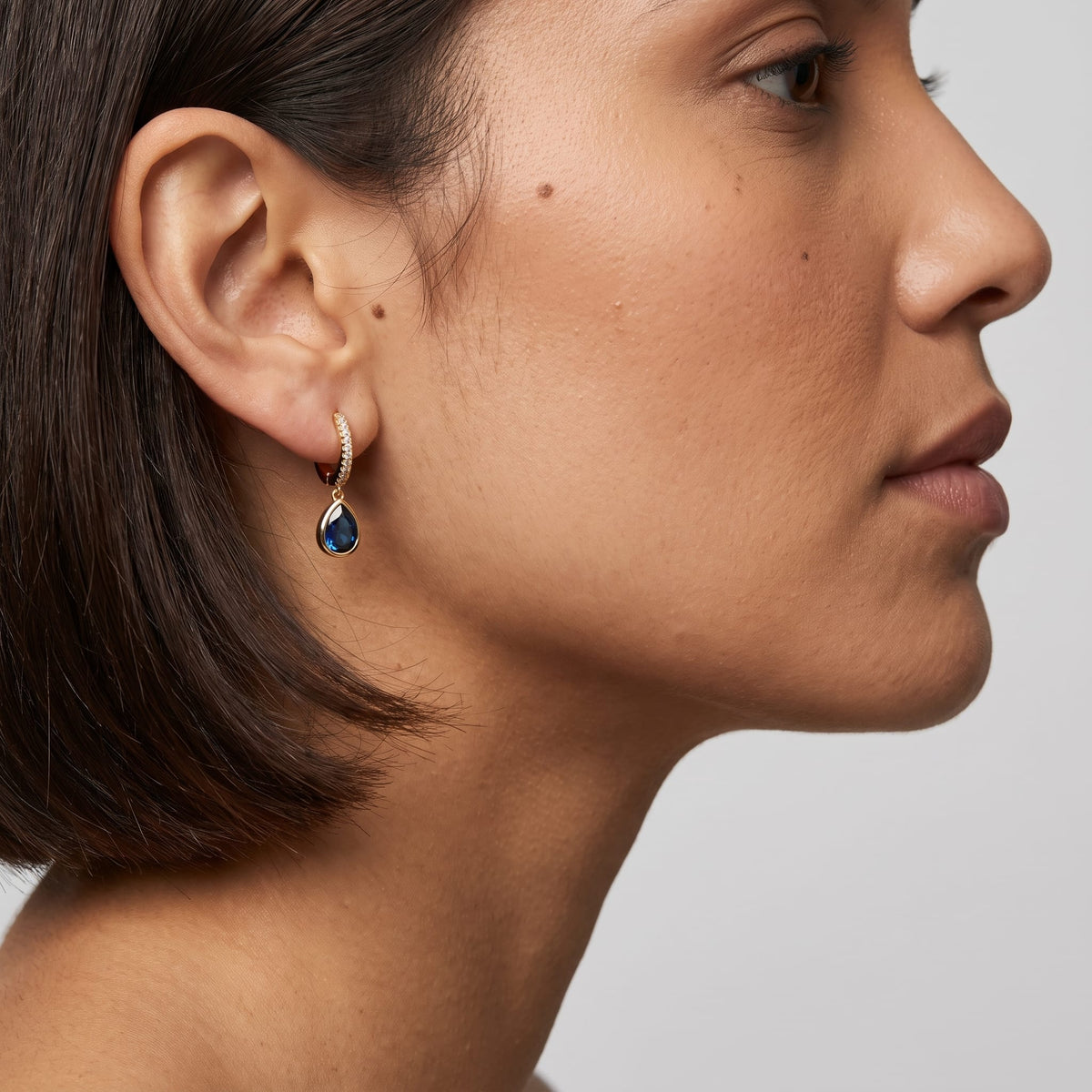 Woman wearing the Paola blue teardrop gold earrings on the ear in profile view