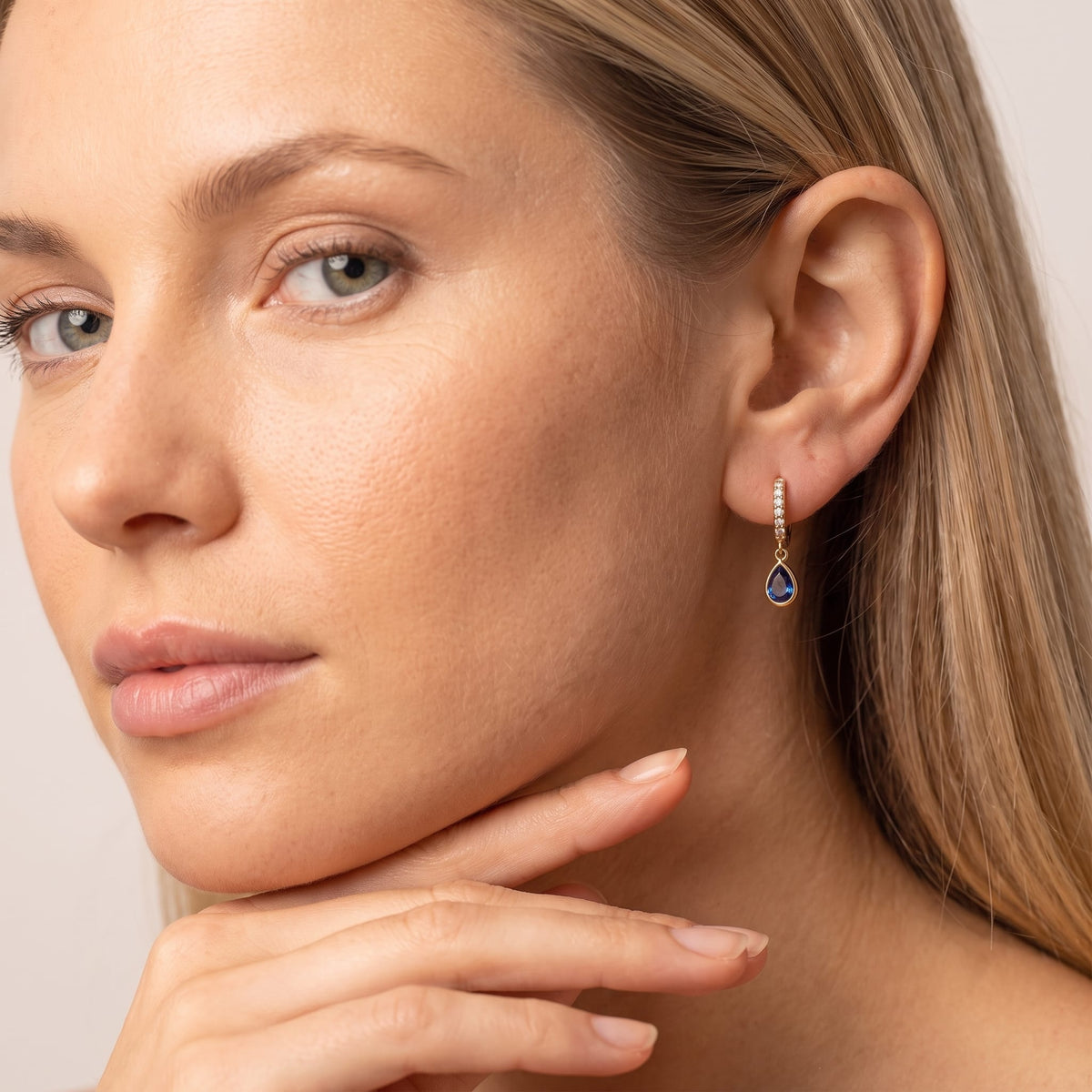 Woman wearing the Paola blue teardrop gold earrings on the ear with hand under chin