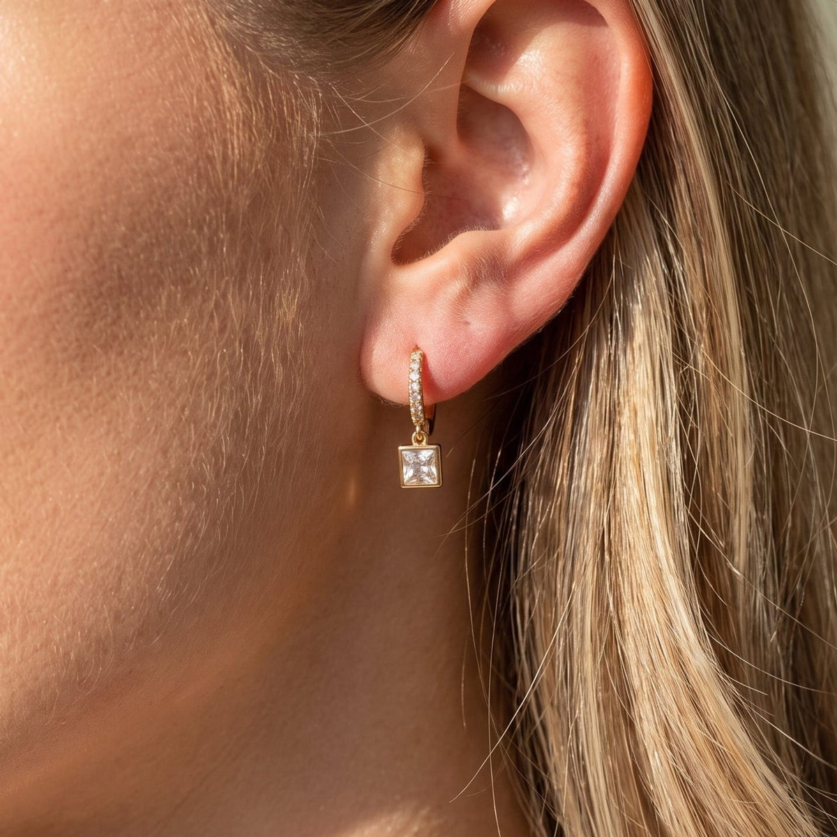 Woman wearing the Paola crystal square gold earrings on the ear