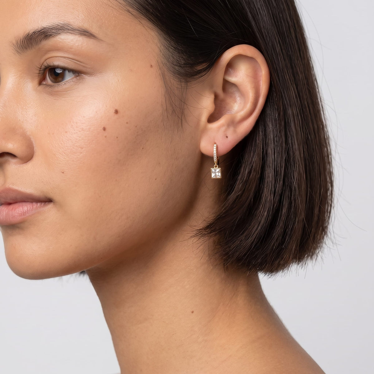 Woman wearing the Paola crystal square gold earrings on the ear with short dark hair