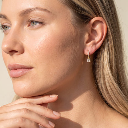 Woman wearing the Paola crystal square gold earrings on the ear resting hand under chin