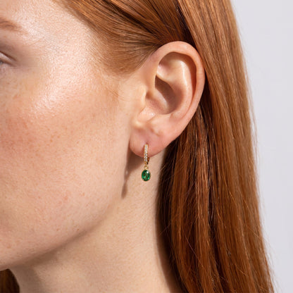 Wider view of a woman wearing the Paola green oval gold earrings on the ear