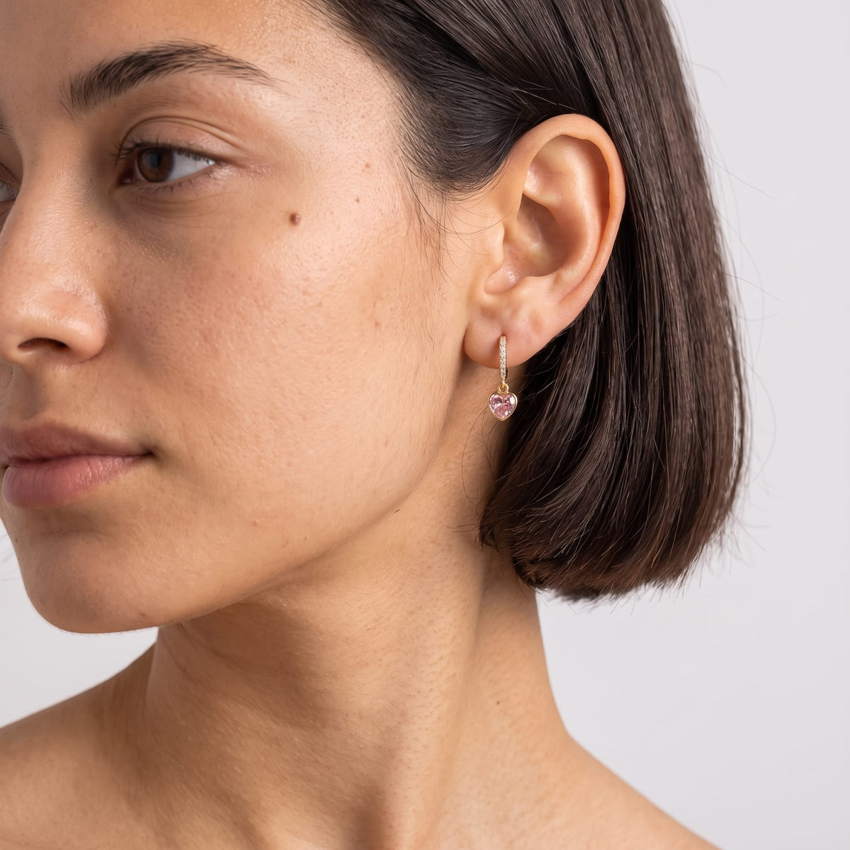 Woman wearing the Paola pink heart gold earrings on the ear in profile view