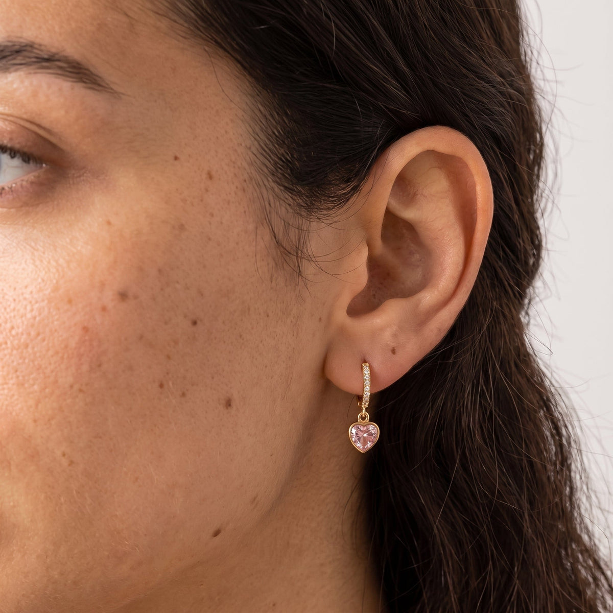 Wider view of a woman wearing the Paola pink heart gold earrings on the ear