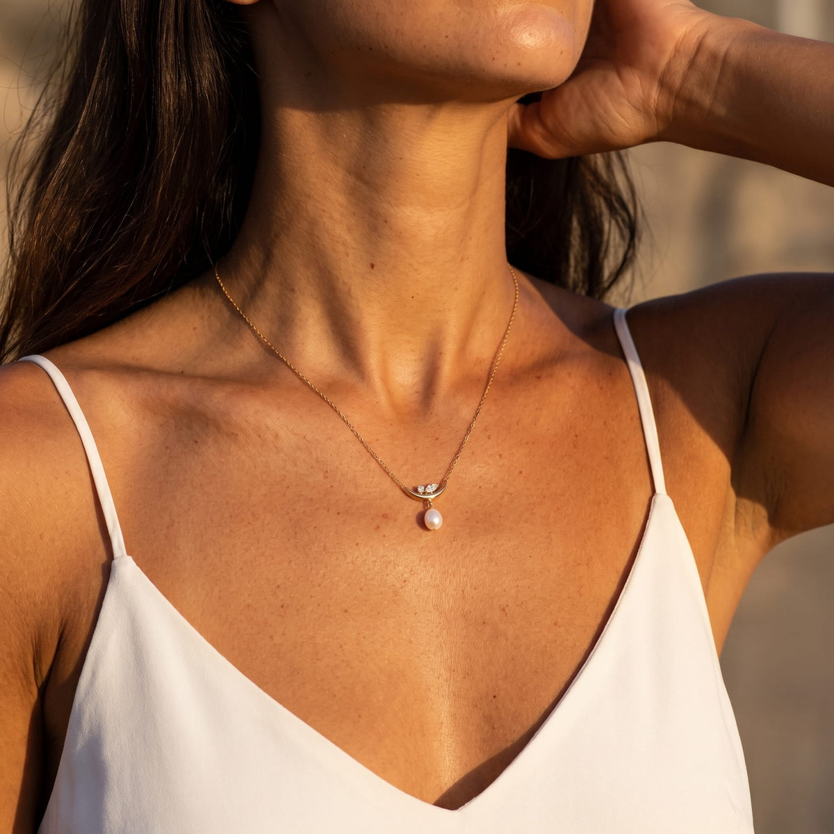 Woman wearing the Pauline moon pearl gold necklace at the collarbone in warm golden sunlight