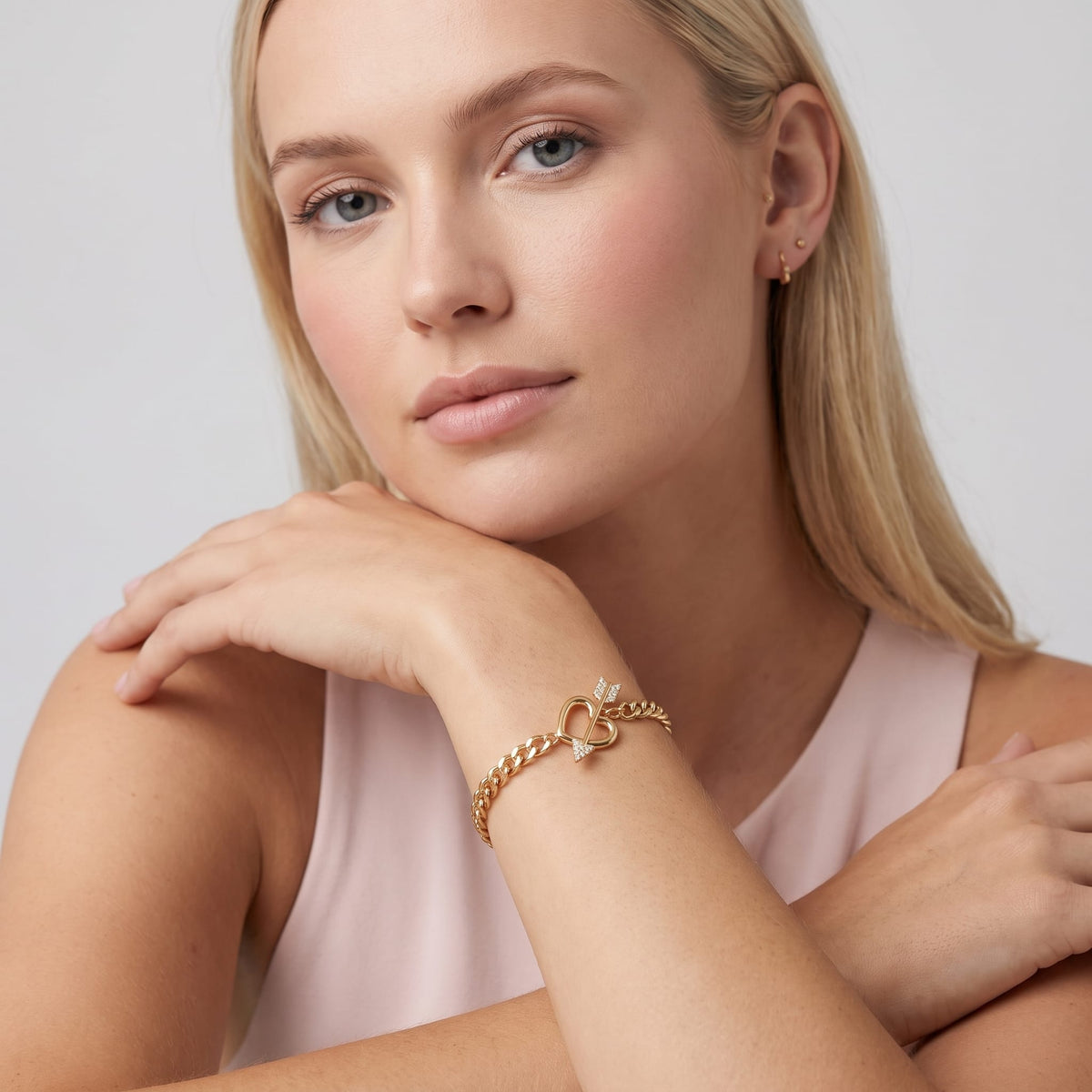 Woman wearing the Rafaella heart arrow gold bracelet on the wrist resting her chin in studio lighting