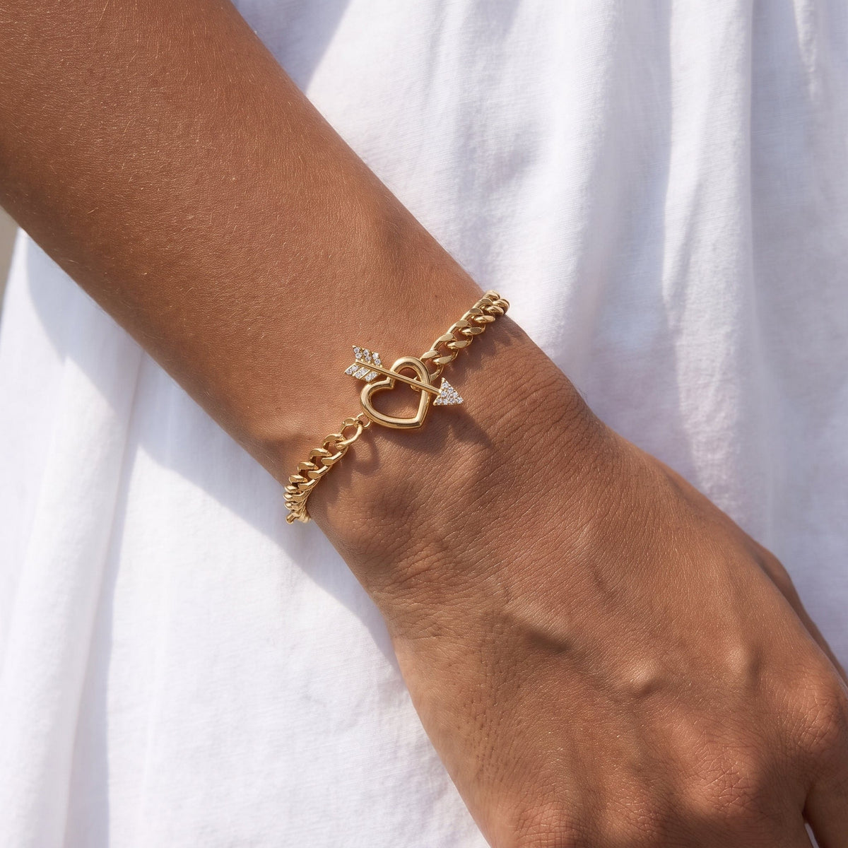Wider view of a woman wearing the Rafaella heart arrow gold bracelet on the wrist