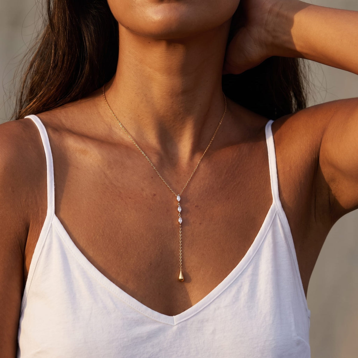 Woman wearing the Rafaella marquise teardrop gold necklace at the collarbone in a white tank top