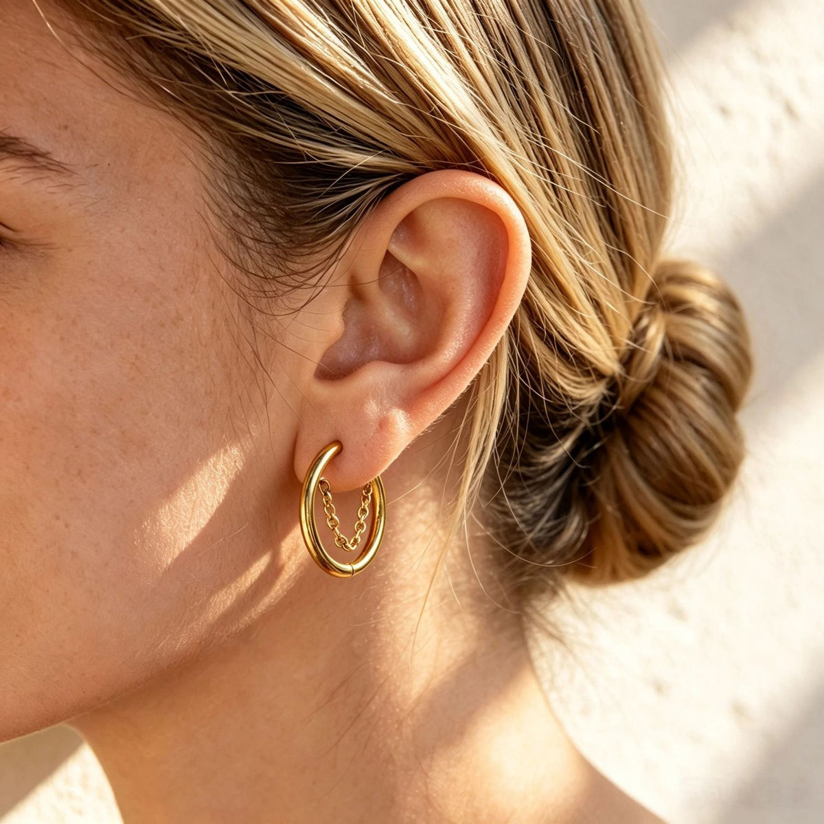 Woman with a low bun wearing the Romy chain hoop gold earring in the lobe, warm sunlight