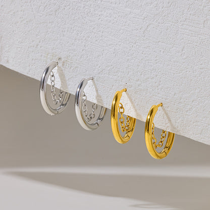 Gold Romy chain hoops hanging from a textured white ledge to the right of the silver pair