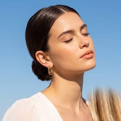 Woman wearing the Romy chain hoop gold earrings on the ear, tilted upward against a clear blue sky