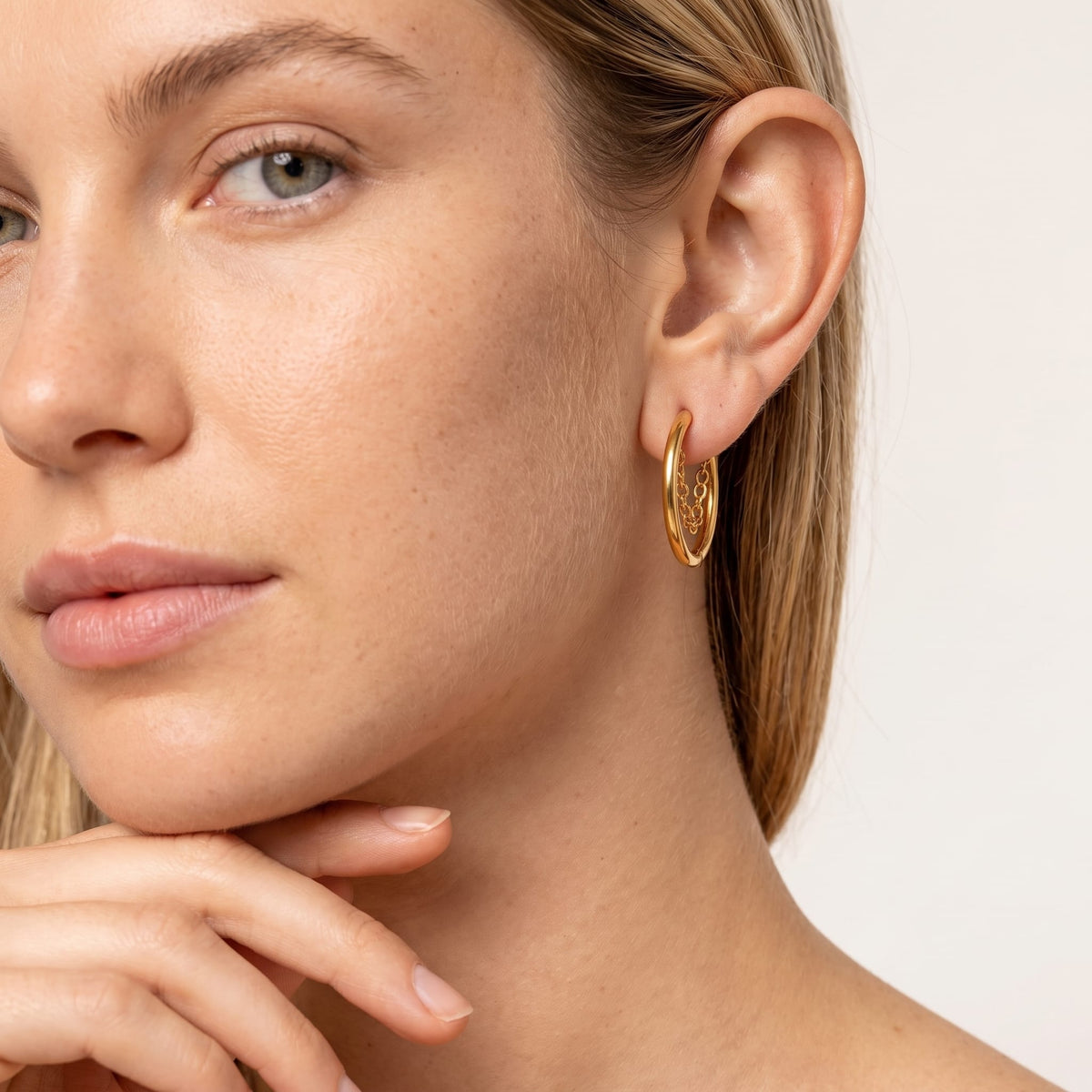 Woman wearing the Romy chain hoop gold earrings on the ear, resting her chin on her hand