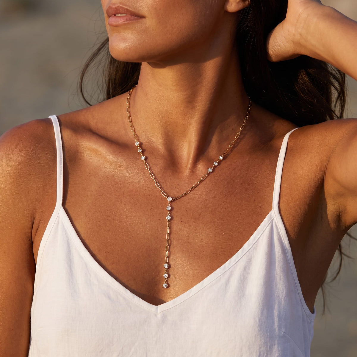 Woman wearing the Rosalba paperclip lariat gold necklace at the collarbone in a white top