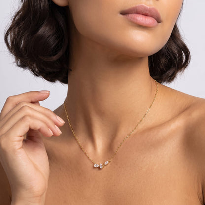 Woman wearing the Rosalie pear cluster gold necklace at the collarbone while touching her hand to her neck