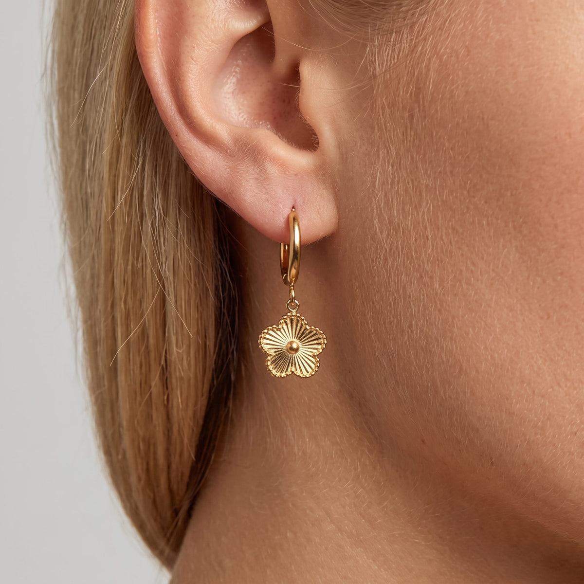 Woman wearing the Rowena gold hoop with a fluted five-petal flower charm hanging below