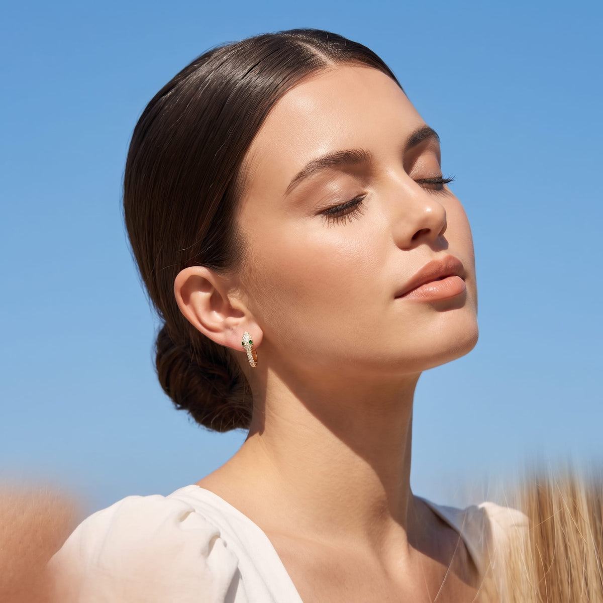 Woman wearing the Sabine pavé snake gold earrings on the ear against blue sky