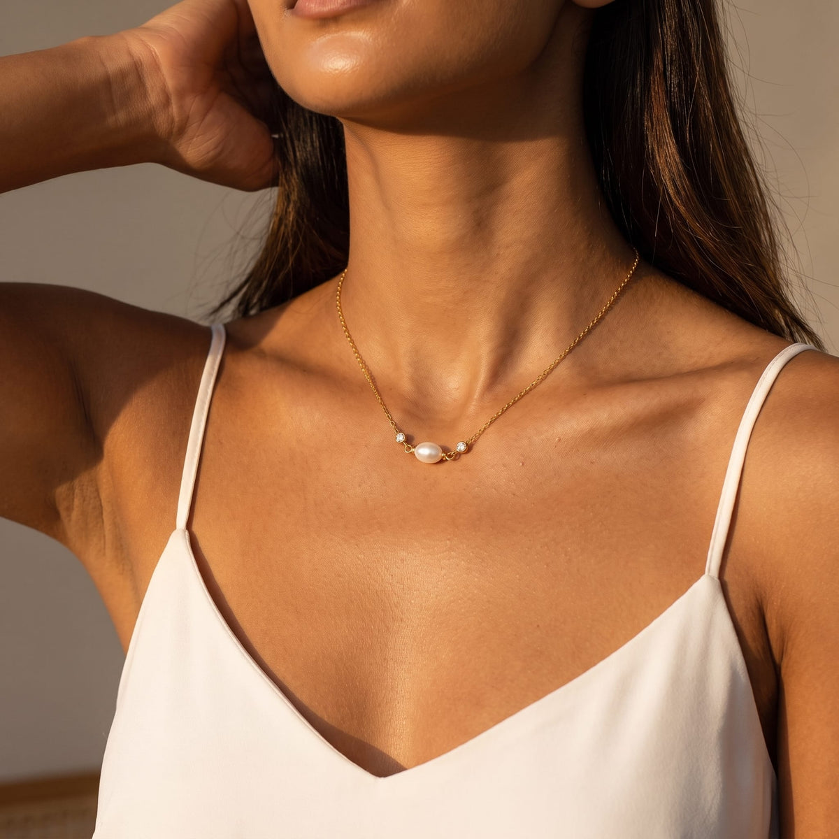 Woman wearing the Serena single pearl gold necklace at the collarbone wearing a white camisole