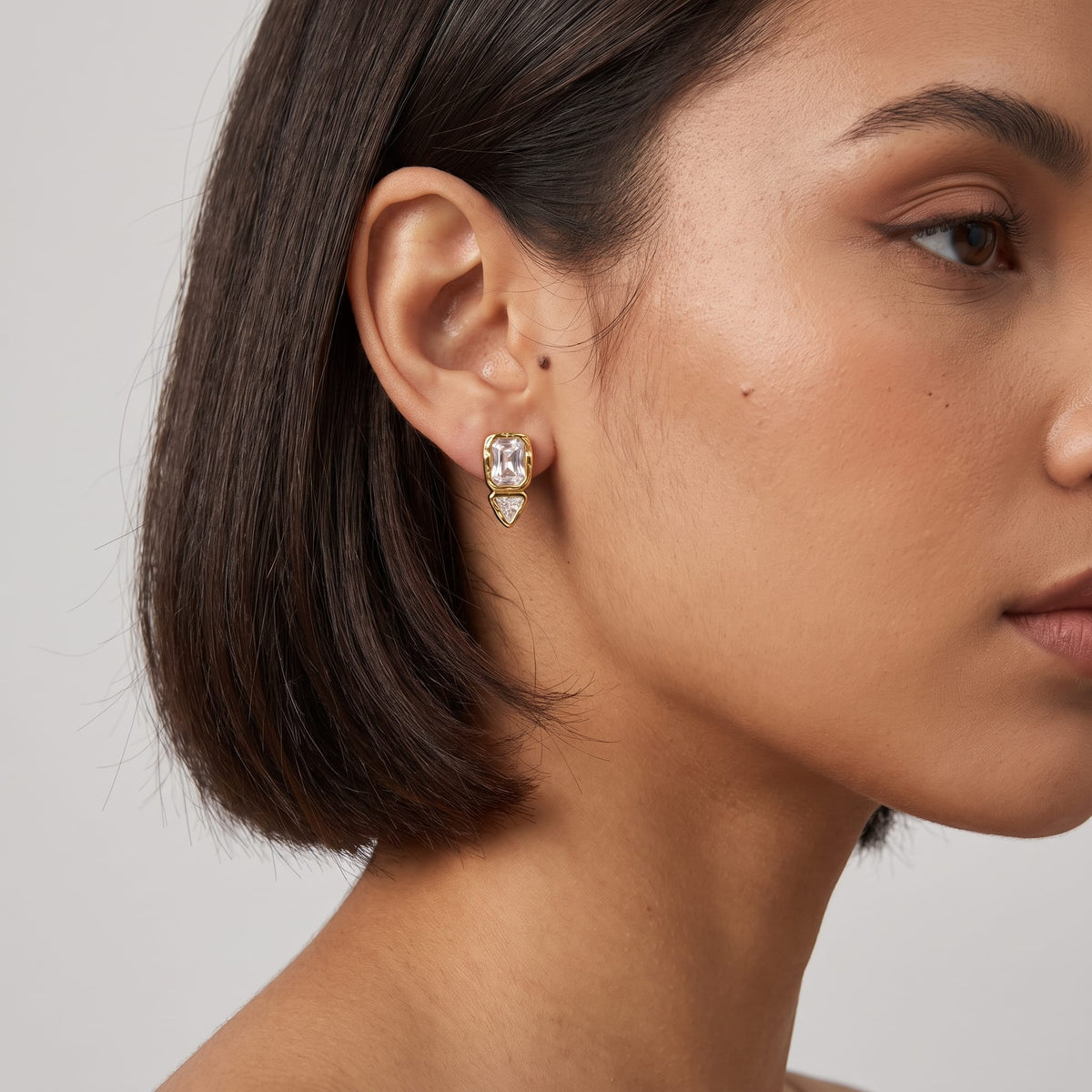 Woman wearing the Sidonie emerald-cut crystal gold earrings on her earlobe with short dark hair