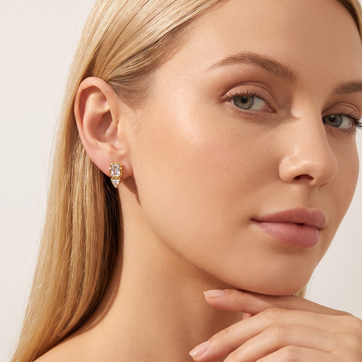 Woman wearing the Sidonie emerald-cut crystal gold earrings on her earlobe resting hand near chin