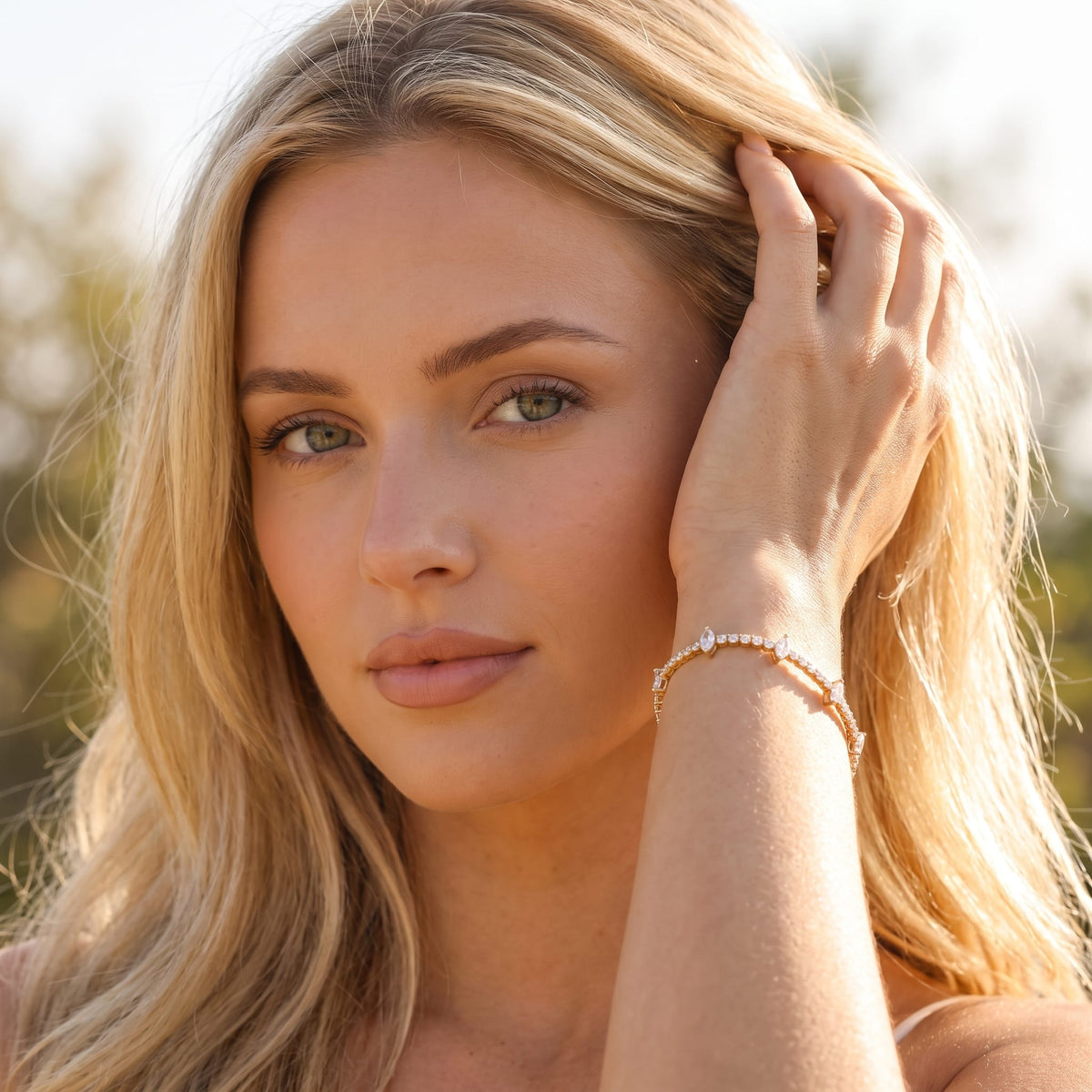 Woman wearing the Sienna marquise tennis gold bracelet on the wrist touching her hair outdoors
