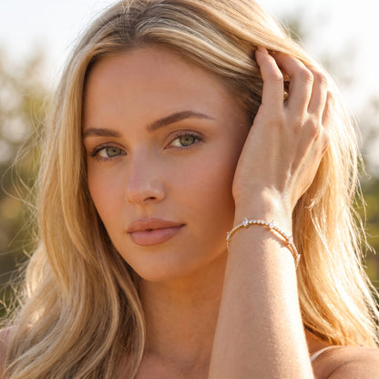 Woman wearing the Sienna marquise tennis gold bracelet on the wrist touching her hair outdoors