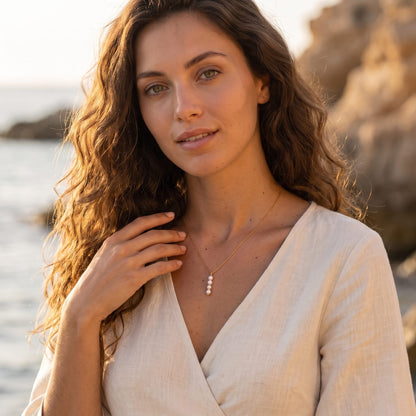 Woman wearing the Simone stacked pearl gold necklace at the collarbone outdoors in a white dress