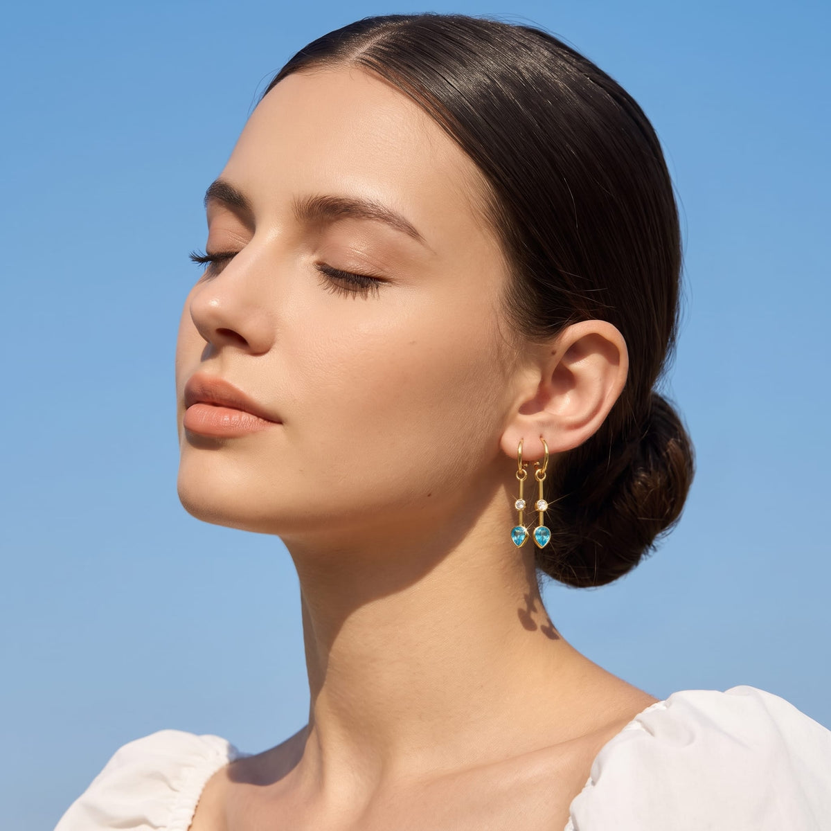 Woman wearing the Sixtine blue bar gold earrings on her earlobe against blue sky
