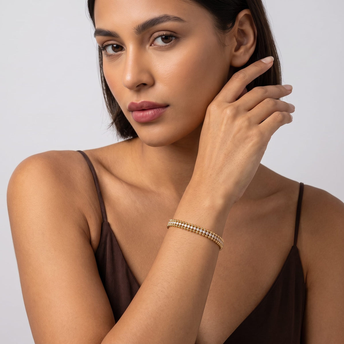 Woman wearing the Sofia bead tennis gold bracelet on the wrist wearing a brown tank top